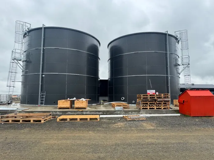 The two completed dark fire water tanks standing side by side on their concrete pad, access stairs up the outside of each