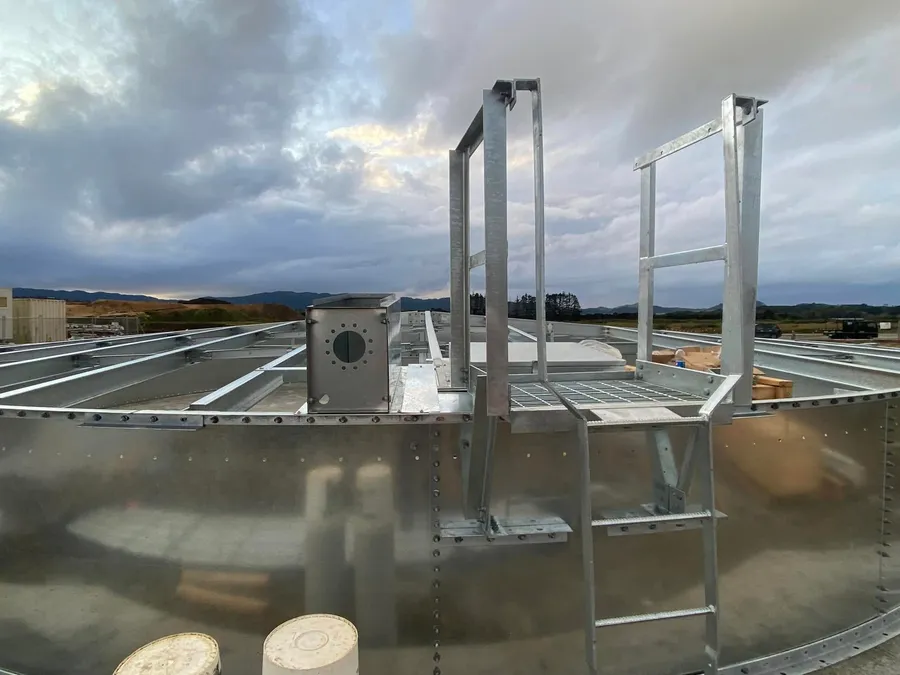 Access platform, handrail and roof hatch on top of a galvanised tank at dusk, roof steel running away behind