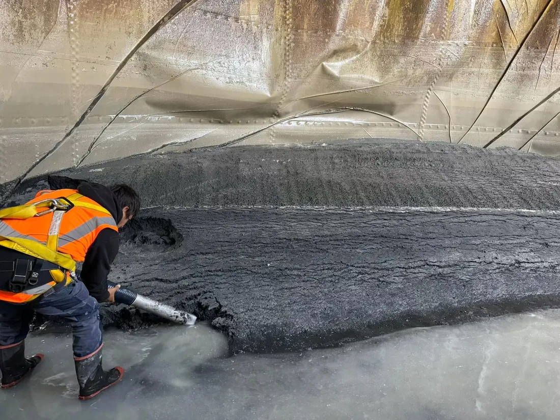 Crew member in a harness clearing sludge from the floor of a tank