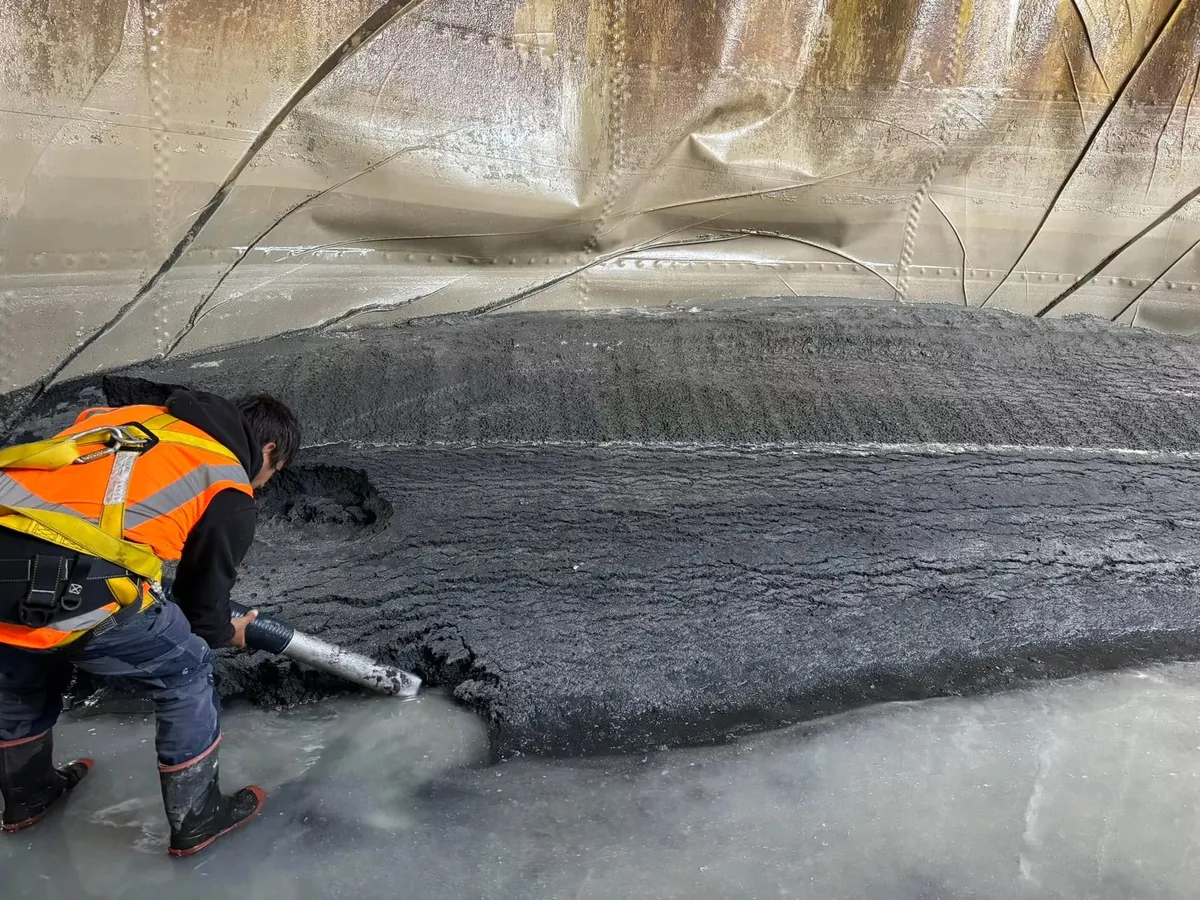 Crew member in harness clearing sludge from a tank floor