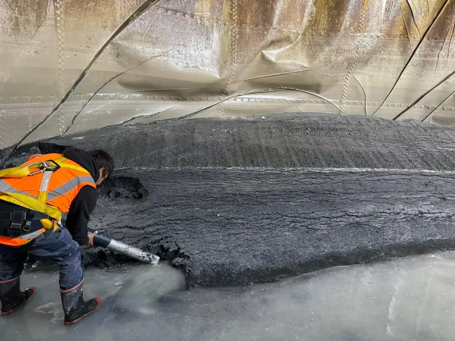 Crew member in harness clearing sludge from a tank floor