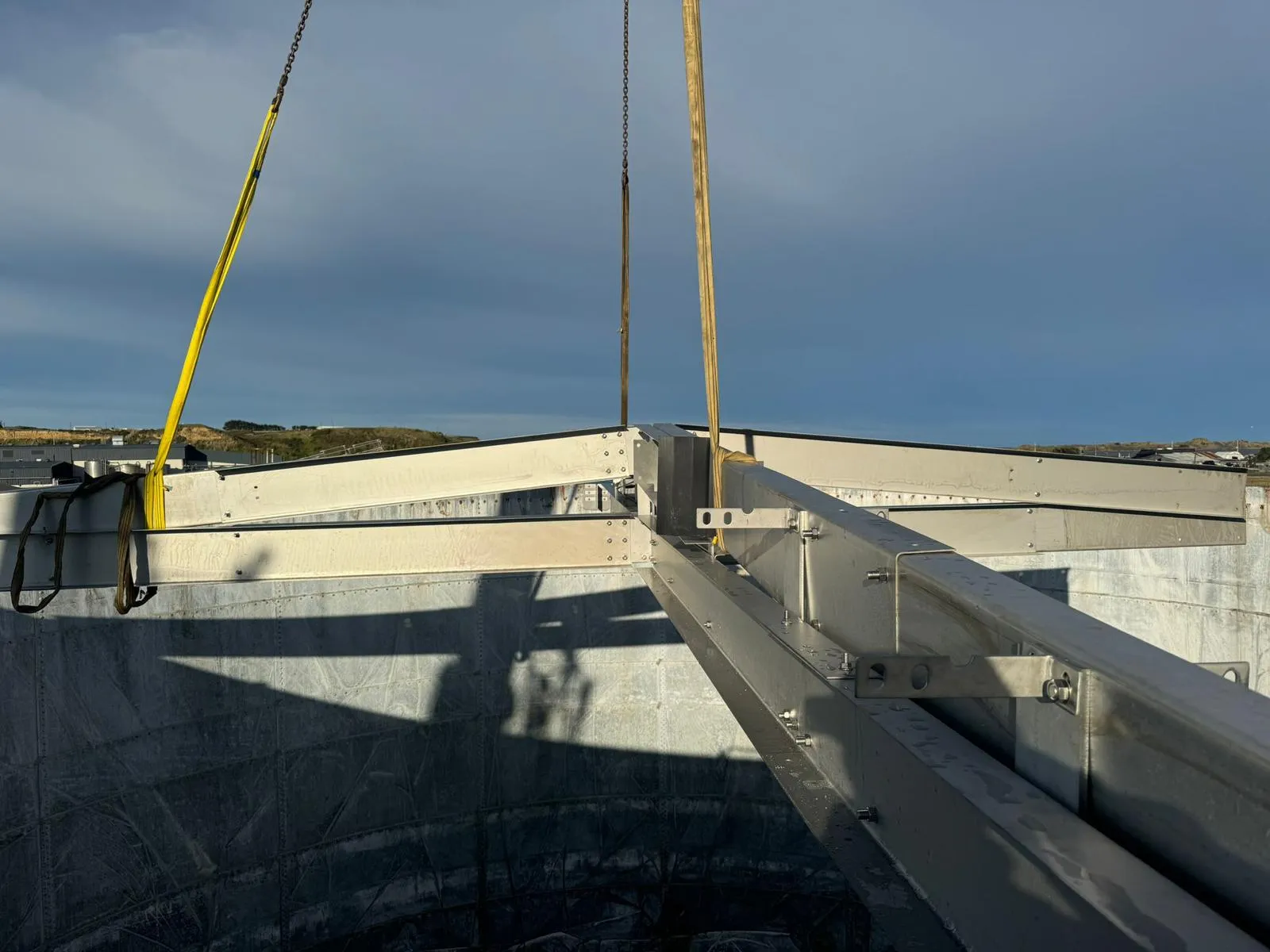 An aluminium roof rafter being lowered onto a tank shell on crane slings