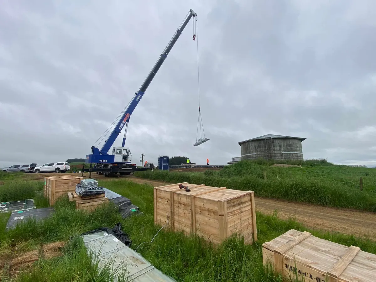 Crane rigged beside stacked crates on a rural tank site under heavy cloud