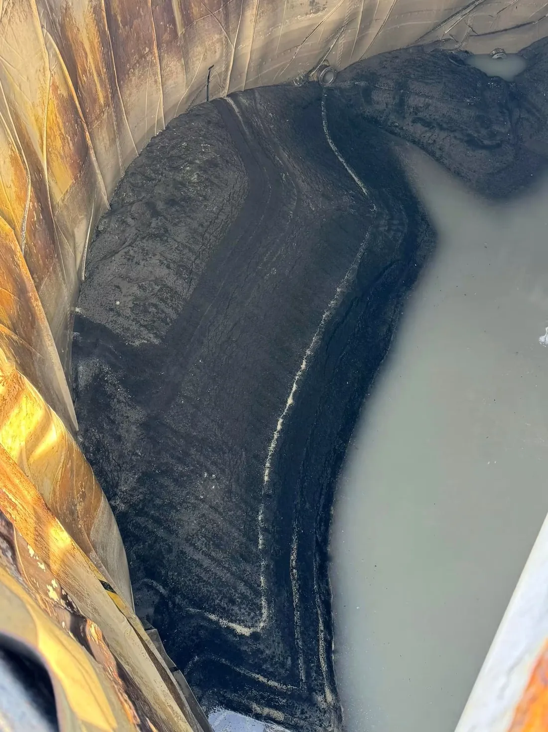 Looking down into a tank at heavy sludge banked against a failed and stained liner