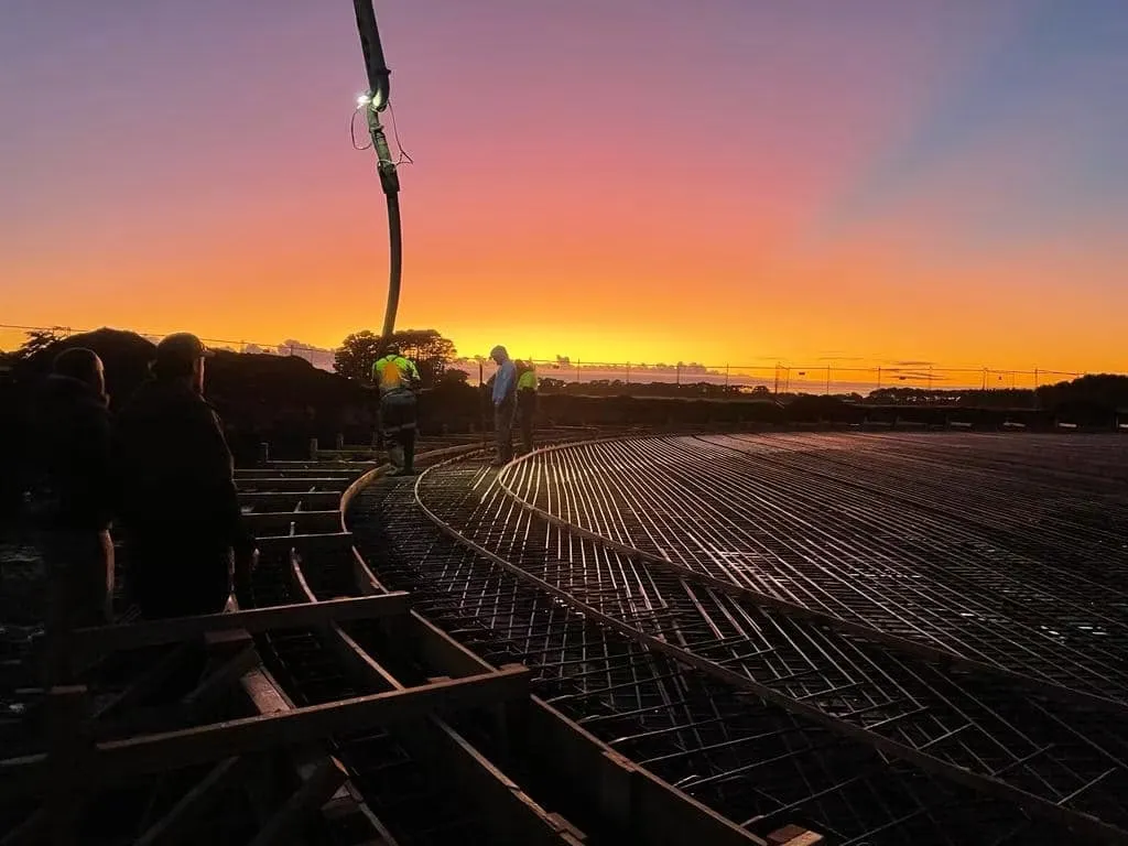 Reinforcing steel laid out for a tank foundation at sunset with the crew still working