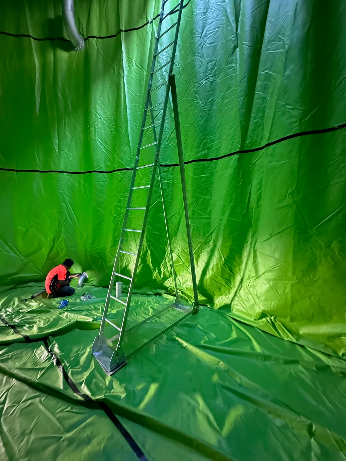 Crew member fitting an outlet inside a tank lined in bright green membrane
