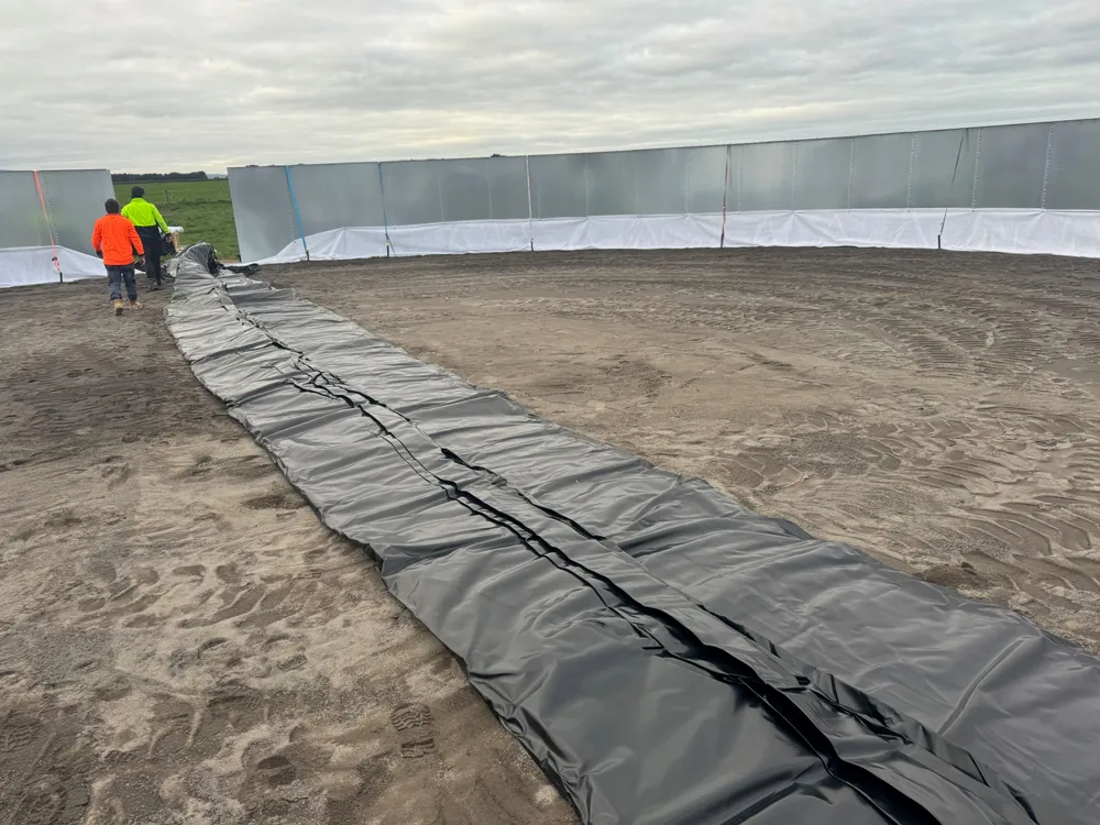 Liner being rolled out inside a bolted tank shell on a rural site, crew and paddock behind