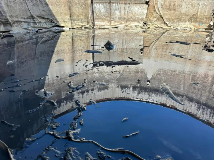 Settled sludge lying in ridges across the old liner under shallow standing water