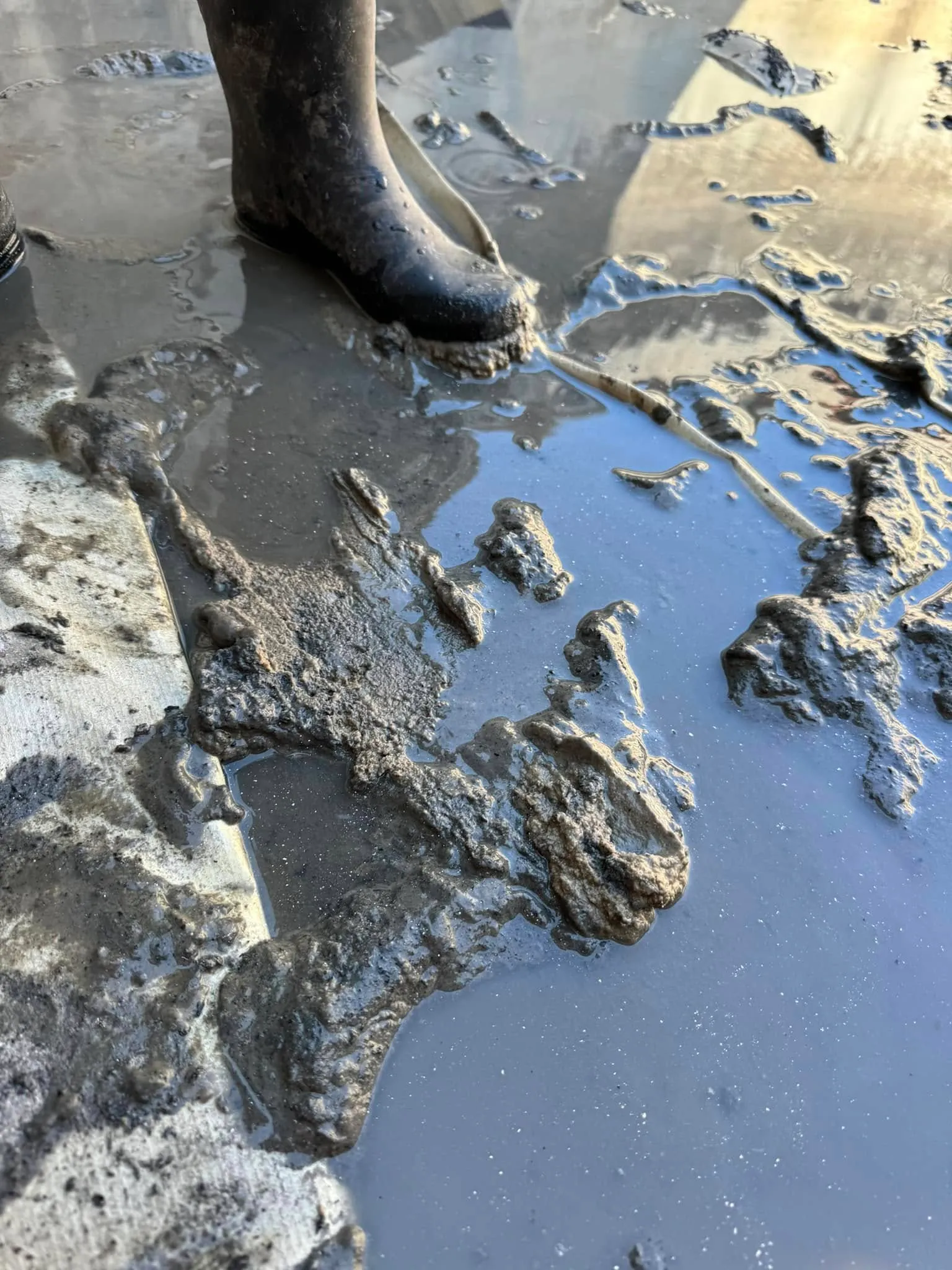 A crew member's gumboots standing in settled sludge on the floor of the tank