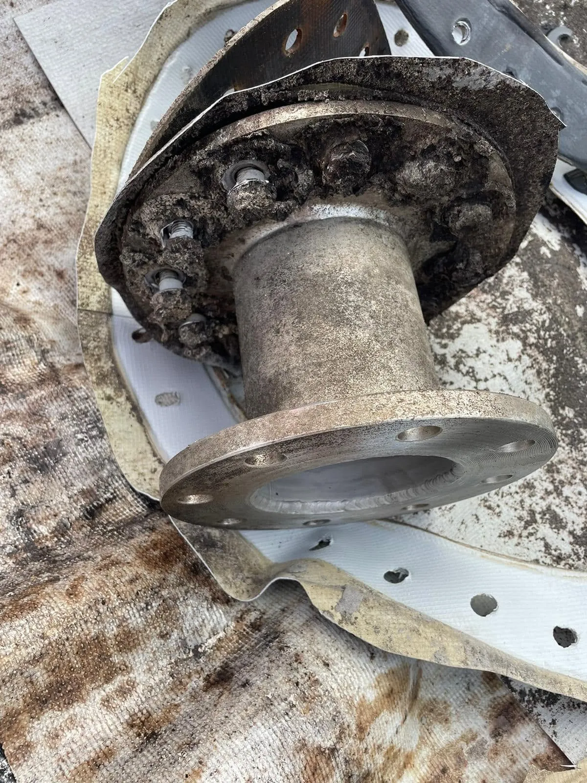 A heavily corroded outlet flange cut out of the tank, resting on the old liner it came through