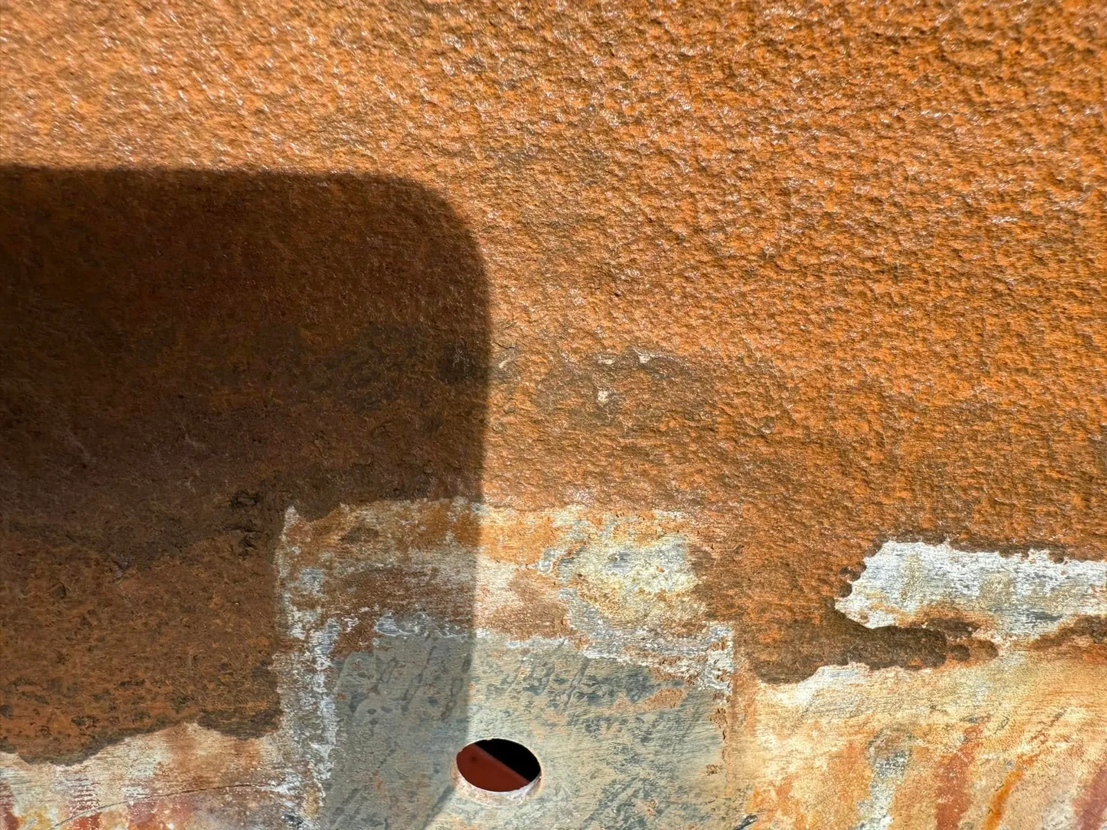 Close detail of a corroded tank panel, the coating flaked back to bare rusted steel around a bolt hole