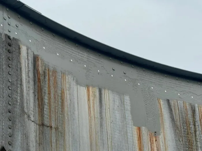Rust streaking down a weathered tank wall, with fresh grey coating going on along the top rail