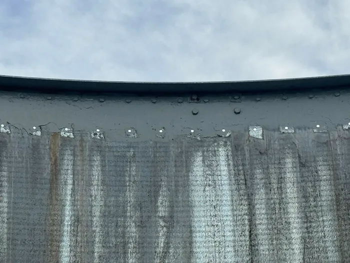 The weathered outside wall of the tank under an overcast sky, streaked the full height of the panels