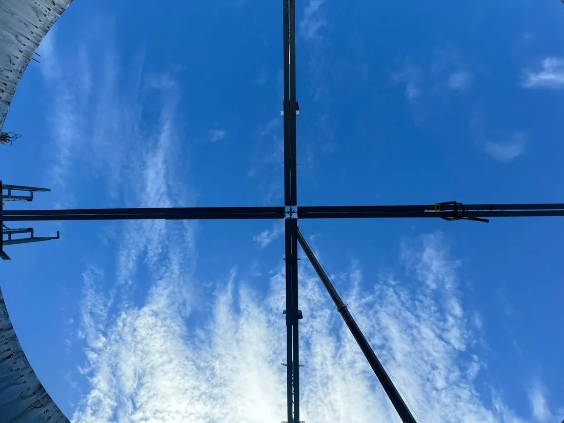 Looking up at steel roof rafters crossing open sky from inside a tank shell