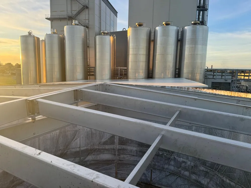 Row of process silos at a plant, seen over tank roof steelwork at dawn